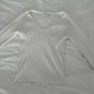 Vit ribbad långärmad topp  - Vit långärmad topp med ribbad struktur och v-ringad hals. Toppens material är stretchigt och sitter snyggt på kroppen. Perfekt att styla med jeans eller kjol för en clean look.