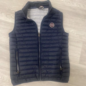 Mörkblå dunväst från Colmar - Säljer en mörkblå dunväst från Colmar med quiltad design och dragkedja framtill. Västen har två fickor med dragkedja och en hög krage. Insidan är vit och västen har en klassisk Colmar-logga på bröstet. Passar för dig som är 155-165cm Perfekt för lager-på-lager under kyliga dagar. Köpte den från kidsbrandstor för 2300kr mitt pris 700kr inga defekter. Pris går att diskuteras. Skriv till mig vid minsta lilla fundering 