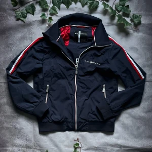 Sail Racing Race Jacket – Storlek S - Sportig och stilren jacka från Sail Racing, känd för sin marina design och höga kvalitet.  🎨 Färg: Marinblå med röda och vita detaljer 📏 Storlek: S 📐 Mått: (kan läggas till vid behov) ♻️ Skick: Mycket bra – sparsamt använd, inga defekter 🧵 Material: 100% Nylon (yttertyg), polyesterfoder  ‼️ Skickas dagen efter köpet genomförs! ‼️ 