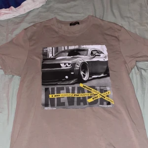 Beige t-shirt med biltryck Highlander - Säljer en beige t-shirt från Highlander i storlek XXL med coolt tryck på framsidan av en sportbil och texten 'NEVADA' samt gula detaljer. T-shirten har rund hals och korta ärmar, perfekt för dig som gillar streetstyle och bilar.