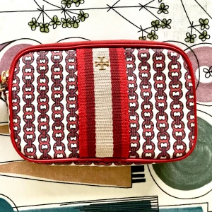 Randig handväska från Tory Burch - Snygg handväska från Tory Burch med rött och vitt randigt mönster och kedjedetaljer. Väskan har guldfärgad logga framtill och dragkedja upptill. Tillverkad i bomull med röda kanter och insida. Perfekt storlek för det viktigaste.