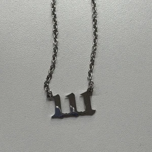 Silverfärgat halsband med '111' - Stilrent halsband i silverfärg med ett coolt '111'-hänge i gotisk stil. Kedjan är tunn och klassisk, perfekt för att ge din outfit en personlig touch. Passar dig som gillar minimalistiska smycken med edge.