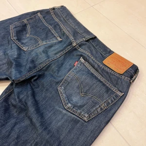 Levi's 501 mörkblå jeans straight fit - Klassiska Levi's 501 jeans i mörkblå tvätt med raka ben och normal passform. Jeansen har fem fickor, knappgylf och kontrastsömmar. Tillverkade i slitstarkt bomullsjeansmaterial med den ikoniska läderpatchen bak i midjan. Passar perfekt för en utekväll eller att ha till skolan🙌Storlek W34 men passar mer som W33 L32