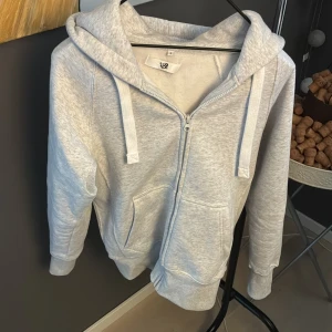 Ljusgrå hoodie med dragkedja, stl S - Ljusgrå hoodie från Russermerch i storlek S. Tröjan har huva med snörning, praktiska fickor framtill och hel dragkedja.