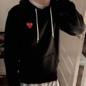 Svart Comme des Garçons PLAY hoodie - Svart hoodie från Comme des Garçons PLAY med vit snörning. Skicket är i helhet bra, OBS‼️har några hål vid armen som knappt syns. Den passar någon som är mellan 160-170cm.