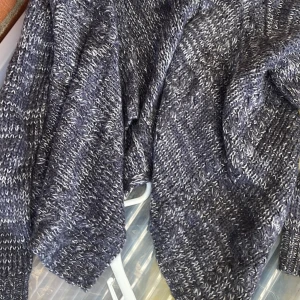 Cardigan till barn 134/140 - Säljer en mysig mörkgrå stickad kofta med vitmelerat mönster. Koftan har långärmade ärmar och är perfekt för kyliga dagar. Den har en loose passform och är superenkel att matcha med jeans eller leggings.