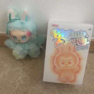 Pop Mart Biginto Energy The Monsters Plush Pendant - Söt samlarfigur från Pop Mart Biginto Energy-serien, The Monsters. Mjuk plysch i mintgrönt med kaninöron och detaljerad ansiktsdesign. Levereras med originalförpackning. Figuren är i mycket gott skick, inga synliga defekter eller slitage.