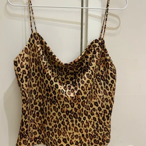  Ny Leopardmönstrad linnetopp från Zara - Säljer en snygg leopardmönstrad linnetopp från Zara i storlek M. Toppen har tunna axelband och en draperad halsringning. Färgerna går i beige, brunt och svart med glansig finish. Perfekt för dig som vill sticka ut med ett djuriskt print. Jag skulle säga att det är en S i storlek.  