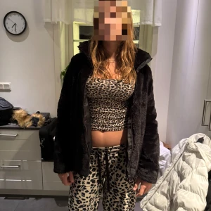 Svart teddyjacka med dragkedja - Mysig svart teddyjacka med dragkedja framtill och hög krage. Jackan har en loose passform och är tillverkad i ett fluffigt, syntetiskt material som känns riktigt skönt. Perfekt för kyliga dagar när du vill vara både varm och snygg.