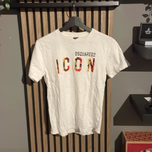 Vit Dsquared2 ICON t-shirt - Snygg vit t-shirt från Dsquared2 med trycket 'ICON' i färgglada bokstäver och Dsquared2-logga ovanför.  De är storlek 152-158. En sjukt skön T-shirt i toppkvalitet!