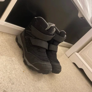 Svarta vinterboots från Viking - Svarta vinterboots från Viking med grå detaljer och breda kardborreband för enkel påtagning. Skorna har grov sula för bra grepp och är fodrade för extra värme. Perfekta för kalla dagar och snö, med slitstarkt syntetmaterial och sportig look.