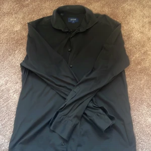 Svart skjorta från Eton slim fit L - Svart skjorta från Eton i slim fit-modell, storlek L. Klassisk design med krage och knappar framtill, långärmad och tillverkad i ett mjukt material. Perfekt för dig som gillar stilrena och enkla plagg med snygg passform. Tröjan är lite urtvättad men har inga hål eller nåt sånt! Va vänlig att ge förslag på pris vid snabbförsäljning