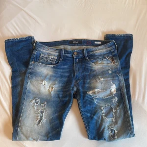 Replay Anbass blå slitna jeans, stl 33 - Säljer ett par Replay Anbass jeans i blå tvätt med coola slitningar och distressed detaljer både fram och bak. Klassisk femficksmodell med Replay-logga på fickan och läderpatch bak. Helt nya och sitter perfekt🤩🤩🤩