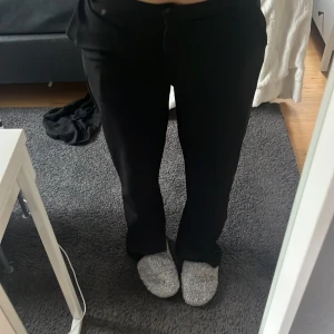 Svarta vida kostymbyxor - Säljer ett par svarta kostymbyxor med raka, vida ben. Byxorna har klassisk passform och stängs med dragkedja och knapp framtill. Perfekta för en clean och stilren look.