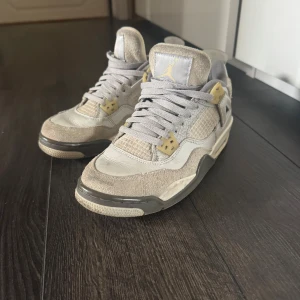 Air Jordan 4 Retro SE Craft sneakers - Säljer ett par Air Jordan 4 Retro SE Craft sneakers i ljusgrå och beige färg med detaljer i gult. Skorna har en mix av mocka och skinn, meshpaneler på sidorna och klassisk snörning. Snygg platt sula och rund tå, perfekt för dig som gillar streetwear och vill sticka ut. Låda medföljer