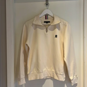 Ljus begie/ vit half zip tröja Tommy Hilfiger - Snygg vit långärmad tröja från Tommy Hilfiger med half zip och broderad TH-logga på bröstet. Tröjan har klassiska Hilfiger-detaljer i rött, vitt och blått vid nacken och en liten logga på ärmslutet. Mjuk bomullskvalitet och normal passform. Ett par fläckar på kragen som knappt syns när man ser den i verkligheten, detta visas på sista bilden. Och kragen är oftast vikt så inget någon märker. Nypris ca 2400💸