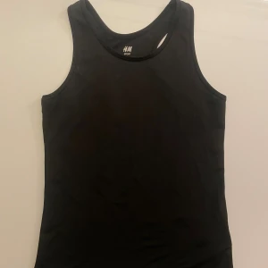 Svart sportig linnetopp från H&M - Svart linnetopp från H&M Sport, perfekt för träning. Modellen är ärmlös med klassisk racerback och rund halsringning. Materialet är mjukt och stretchigt polyester som andas bra. Enkel och stilren design utan mönster eller detaljer.