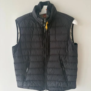 Svart dunväst från Parajumpers L - Svart quiltad dunväst från Parajumpers i storlek L. Västen har hög krage, dragkedja framtill och två sidofickor med dragkedja. Märkespatch på ryggen och insidan, samt gul detalj vid halsen. Perfekt för lager-på-lager och chill stil.