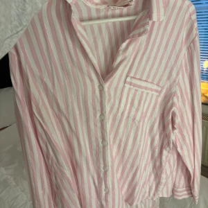 Rosa och vit randig pyjamaströja - Victoria's Secret - Snygg skjorta från Victoria's Secret i storlek M med rosa och vita vertikala ränder och diskreta glittriga detaljer. Skjortan har klassisk krage, knappstängning framtill och en bröstficka. Den är både luftig och skön vilket gör den bekväm att sova i. Endast prövad!💗