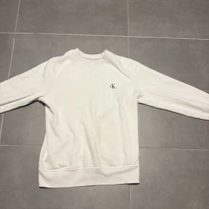 Vit sweatshirt från Calvin Klein Jeans - Vit sweatshirt från Calvin Klein Jeans med broderad CK-logga på bröstet och Calvin Klein Jeans-text på ärmslutet. Tröjan har rund hals, ribbade muddar och är tillverkad i mjuk bomull. Perfekt för en clean och stilren look.