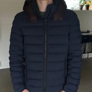 Colmar pufferjacka  - Säljer en mörkblå pufferjacka från Colmar med avtagbar huva och bruna detaljer. Bra skick använd ett par gånger förra vintern sen dess inte använd. Storlek M men passar även S. Pris kan diskuteras och tveka inte skriva om ni undrar nåt!