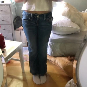 Blå bootcut jeans från Ginatricot - Snygga blå jeans från Ginatricot med bootcut passform och låg midja. Klassisk femficksmodell med silverfärgade knappar och detaljerade sömmar. Jeansen har en lätt tvättad look och är tillverkade i mjukt denimtyg som sitter skönt.