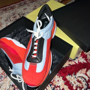 J.Lindeberg sneakers - Säljer ett par snygga sneakers från J.Lindeberg med ett fräck mix av rött, ljusblått, svart och orange. Skorna har en platt sula från Vibram, snörning och detaljer i mocka och syntet. Perfekt för dig som gillar att sticka ut med unika. 🛸Storlek 44/45.