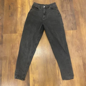 Svarta högmidjade jeans - Svarta jeans med hög midja och klassisk femficksdesign. Jeansen har en rak passform som smalnar av vid anklarna och stängs med dragkedja och knapp. Perfekta för en avslappnad och trendig look.