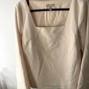 Beige långärmad blus från H&M - Säljer en stilren beige blus från H&M i storlek S. Blusen har en fyrkantig halsringning och långa ärmar, vilket ger en modern och clean look. Materialet är mjukt och känns skönt mot huden. Perfekt för dig som gillar minimalistisk stil.