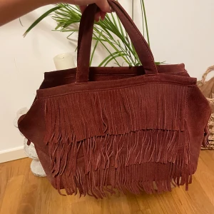 Snygg röd mockaväska med fransar - Sååå snygg, inga defekter har bara tröttnat 💕rymmer mac book 13’ och flera skolböcker, har en innerficka med dragkedja 🥰 inga fransar baktill. Kan ta flera bilder vid intresse 😊😊😊