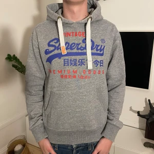 Grå Superdry hoodie  - Skön superdry hoodie i storlek M. Modellen är 187cm. Skriv vid minsta fundering