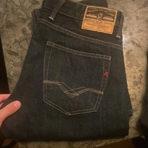Replay jeans mörkblå 33/32 - Snygga mörkblå Replay jeans med klassisk femficksdesign och kontrastsömmar. Märkespatch i läder baktill och diskret Replay-logga på fickan. Jeansen har normal passform och är tillverkade i slitstarkt denimmaterial. Perfekt för dig som gillar stilrena och tidlösa jeans.