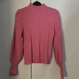 Rosa ribbad stickad tröja från ONLY - Säljer en rosa stickad tröja från ONLY med ribbad struktur och långärmade puffärmar. Tröjan har en hög hals och är gjord i ett mjukt material som känns skönt mot huden. Perfekt för dig som gillar färg och vill ha en mysig look.