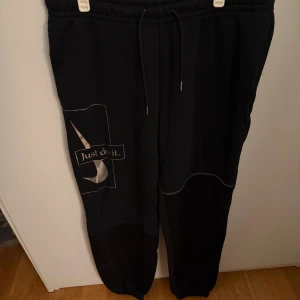 Svarta mjukisbyxor Nike  - Svarta mjukisbyxor från Nike med silverfärgad 'Just do it.'-logga och swoosh på benet. Byxorna har snörning i midjan, muddar vid benslut och broderad Nike-text baktill. Perfekta för chill eller träning. Säljer då de inte används längre, men är gott skick!💕