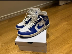 Nike Air Jordan 1 blå och vita sneakers - Nike Air Jordan 1 sneakers i blått och vitt med klassisk high-top siluett. Skorna har perforerad tå, snörning och ikoniska Jordan-loggor på sidan och plösen. Tillverkade i skinn med vit sula och blå detaljer, PRIS KAN DISKUTERAS TVEKA INTE!!