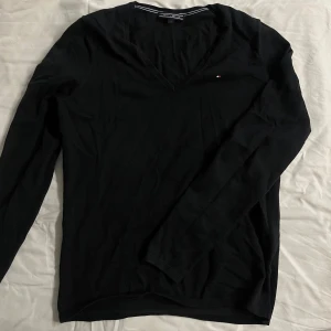 Svart v-ringad tröja Tommy Hilfiger - Svart v-ringad tröja från Tommy Hilfiger i storlek S. Långärmad och tillverkad i mjuk bomull, perfekt för en clean och stilren look. Jag har inte riktigt använt den då för den är ganska stretchig och den va för stor för mig.