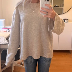 Beige stickad tröja med loose fit - Mysig beige stickad tröja med loose passform och långa ärmar. Tröjan har ribbade muddar vid ärmslut och nederkant, perfekt för att hålla värmen under kyliga dagar. Enkel och stilren design som är lätt att matcha med jeans eller andra favoritplagg.