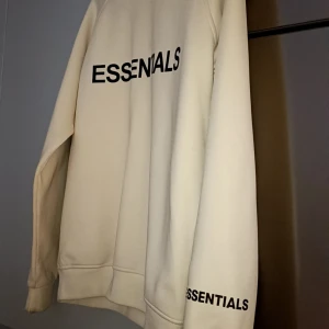 Beige Essentials sweatshirt i medium - Säljer en beige sweatshirt från Essentials i storlek M. Tröjan har svart tryck med loggan på bröstet och ärmen, rund hals och lång ärm. Materialet är mjukt och känns som polyester, perfekt för dig som gillar cleana och stilrena plagg. Riktigt fin tröja passar medium o large då den lite stor i storlel tagit väl hand om den i Cirka 6 mån. Säljes för 550 kr köpt för 1299kr