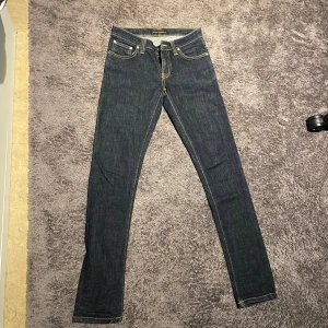 Mörkblå skinny jeans från Nudie Jeans - Snygga mörkblå skinny jeans från Nudie Jeans med klassiska kontrastsömmar och coola broderade detaljer på bakfickorna. Modellen har fem fickor. Perfekt för dig som gillar stilrena och moderna jeans.