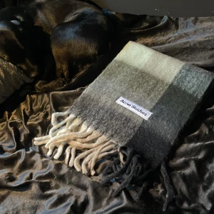 Rutig Acne Studios halsduk i ull - Säljer en stor och fluffig halsduk från Acne Studios med rutigt mönster i grått, svart, beige och vitt. Halsduken har långa fransar.