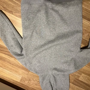 Grå hoodie från Lacoste med dragkedja - Snygg grå hoodie från Lacoste med dragkedja framtill och klassisk krokodillogga på bröstet. Tröjan har huva med snörning och långa ärmar. Perfekt för en chill och sportig stil. Materialet är mjuk bomullsmix som känns skönt mot huden.