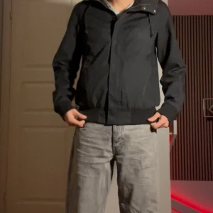 Svart vindjacka från These Glory Days - Svart vindjacka från These Glory Days i storlek small. Jackan har en stilren look med huva, dragkedja framtill och ribbade muddar vid midja och ärmslut. Perfekt för dig som gillar minimalistisk stil och vill ha en jacka som funkar till många outfits.