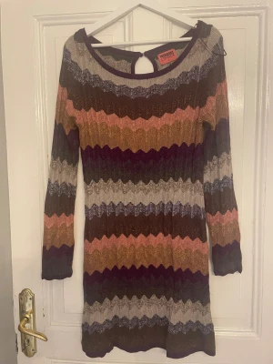 Randig stickad klänning Missoni x Lindex - Superfin stickad klänning från Missoni x Lindex med vågiga ränder i beige, brun, rosa, lila och grå. Modellen är kort med långärmade ärmar och rund hals med en liten öppning bak med knapp. Perfekt för dig som gillar färg och mönster!