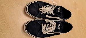 Svarta Vans sneakers strl 41 - Säljer ett par klassiska Vans sneakers i svart med vit sula och vit sidostrip. Skorna har rund tå, platt sula och snörning framtill. Materialet är slitstark canvas och detaljer i mocka. Perfekt för dig som gillar streetstyle och skate.