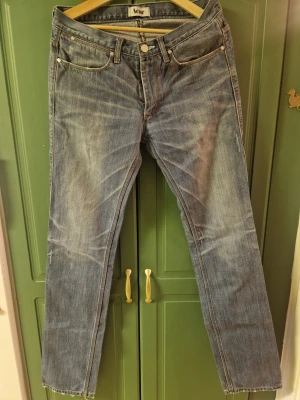 Blå jeans från Acne, Max Stencil 32/34 - Snygga blå jeans från Acne, Max Stencil, i storlek W32/L34 med klassisk femficksdesign och raka ben. Jeansen har ljus tvätt med subtila slitningar, silverfärgade nitar och knapp med Acne-logga. Passar dig som gillar stilrena och tidlösa jeans med normal passform.