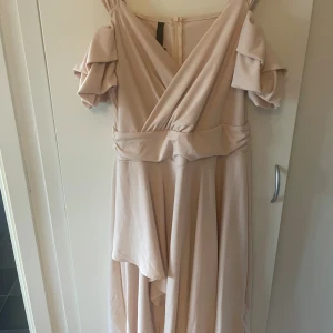 Champagnefärgad långklänning ChicMe XL - Säljer en elegant champagnefärgad långklänning från ChicMe i storlek XL. Klänningen har omlott-v-ringning, volangdetaljer på de korta ärmarna och ett markerat midjeband. Materialet är mjukt och faller snyggt, perfekt för dig som gillar en feminin och flowy stil.