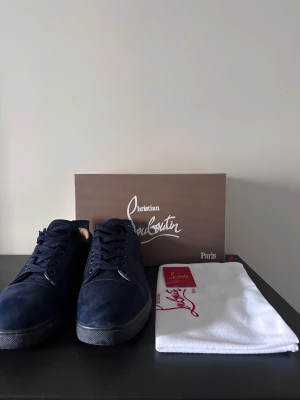 Mörkblå sneakers Christian Louboutin - Snygga mörkblå sneakers från Christian Louboutin i mocka med klassisk röd sula och rund tå. Skorna har snörning och platt sula, levereras med originalkartong och dustbag. Perfekt för dig som vill sticka ut med exklusiva detaljer och lyxig känsla.