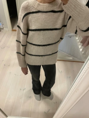 Beige stickad randig tröja Gina Tricot - Mysig stickad tröja från Gina Tricot i beige med svarta horisontella ränder. Tröjan har rund hals, ribbade muddar och lång ärm.