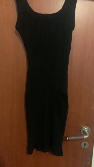 Svart ribbad ärmlös klänning - Snygg svart ribbad klänning med ärmlös design och rund hals. Klänningen har en kroppsnära passform och är tillverkad i ett stretchigt stickat material som sitter skönt. Perfekt för dig som gillar minimalistisk stil och vill ha en enkel men stilren look. Priset kan diskuteras 