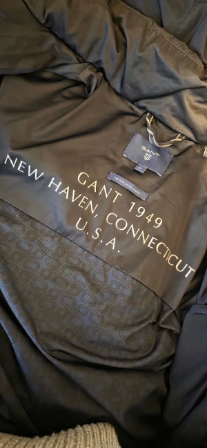 Mörkblå dunjacka från GANT - Snygg mörkblå pufferjacka från GANT, modell Alta Down Jacket. Jackan har huva, dragkedja framtill och två sidofickor med dragkedja Den är i bra skick. 